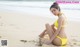 A woman in a yellow bikini sitting on the beach.