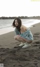 A woman kneeling on a beach with a towel wrapped around her body.