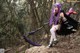 A woman with purple hair holding a bow and arrow.