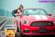 A woman leaning on the hood of a red sports car.