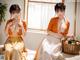 A woman in an orange kimono sitting on a bed next to a basket of fruit.